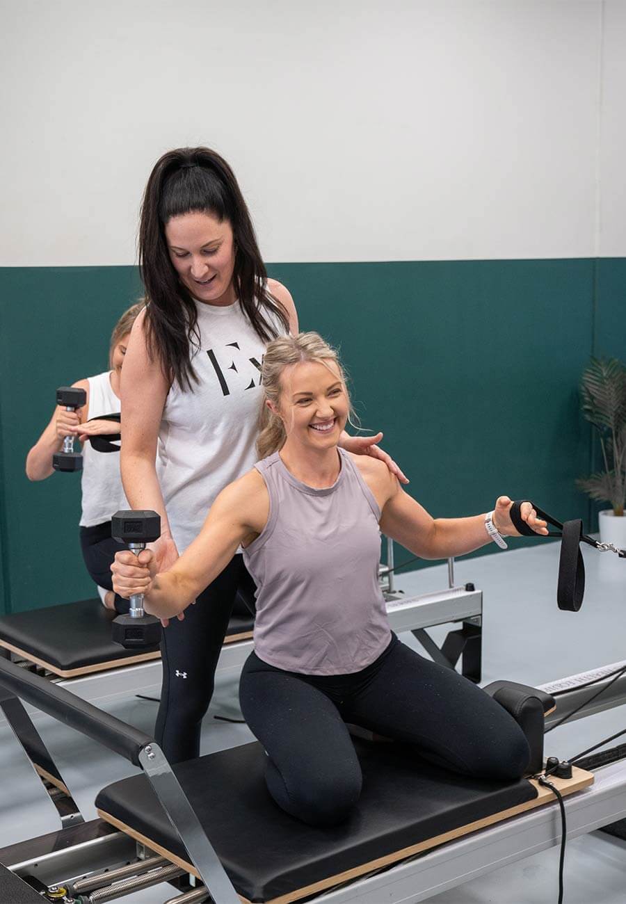 A pilates instructor helping a women with her weights in a reformer class.
